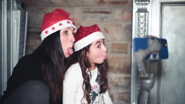 Femme et sa fille à la maison pour Noël portant Santa Hat faisant grimaces devant une caméra vidéo. Appel vidéo avec les parents — Video