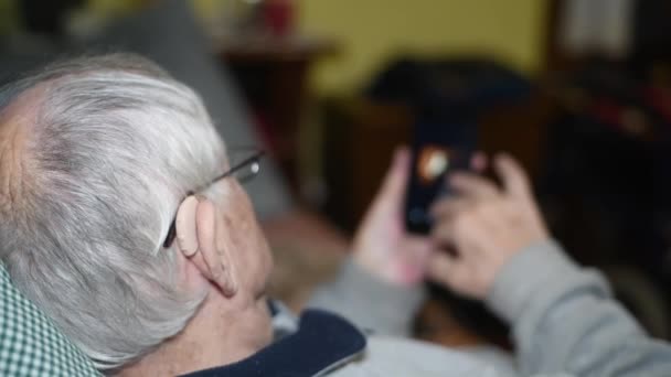 Eldre pensjonert mann på 80-tallet som lente seg mot sofaen og brukte smarttelefon til nyheter. Langsom bevegelse – stockvideo