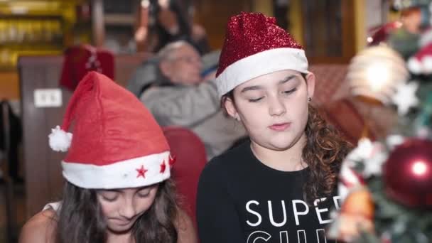 Evde Noel Ağacı 'nı süsleyen iki genç kız arka planda dedesi olan Santa Hat giyiyorlar. Yavaş çekim — Stok video
