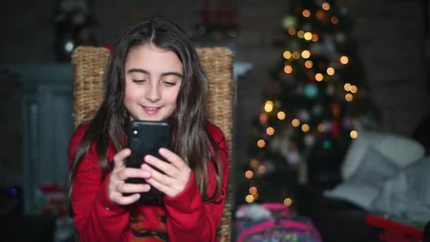 Menina em casa para o Natal sonhando com sua irmã, olhando para o ultra-som do smartphone — Vídeo de Stock