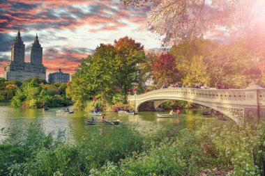 Bow Köprüsü ve Central Park 'taki Göl' ün üzerinde inanılmaz bir gün batımı. New York şehrinin yeşillik renkleri.