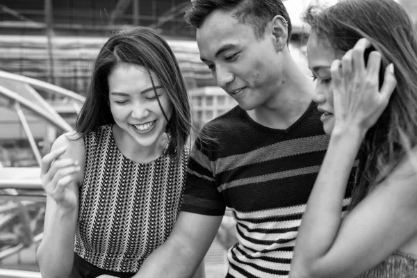 Three young asian friends outdoor in the city looking at something in the boy's hands.