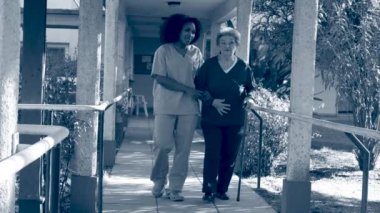 Genç Asyalı kadın doktor hastane bahçesinde koltuk değnekleriyle yaşlı kadına yardım ediyor. Arkadan gelen ışık ışınları