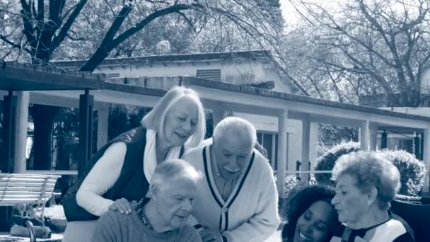 Vista in bianco e nero di due coppie caucasiche anziane che si godono il tempo all'aperto nel giardino di riabilitazione della clinica con medico donna — Video Stock