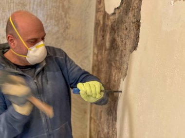 Belediye çalışanı, resim yapmadan önce, bir çekiç ve metal fırçayla, grafik ve yazıtlardan oluşan duvarları temizler..