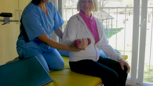 Медсестра помогает пожилой женщине с тренажерами — стоковое видео
