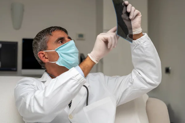 Γιατρός Φορώντας Μάσκα Προσώπου Κοιτάζοντας Ακτινογραφία Οπίσθιου Φωτισμού — Φωτογραφία Αρχείου