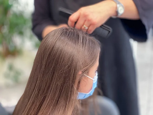 Cute little girl in hairdressing salon wearing face mask during pandemic.