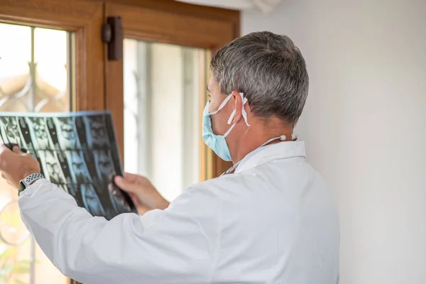 Dokter Met Gezichtsmasker Kijkend Naar Röntgenfoto Verlicht Bij Het Kamerraam — Stockfoto