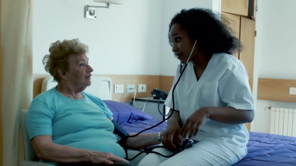 Movimiento lento de la mujer africana médico que mide la presión a la mujer anciana en el hospital — Vídeos de Stock
