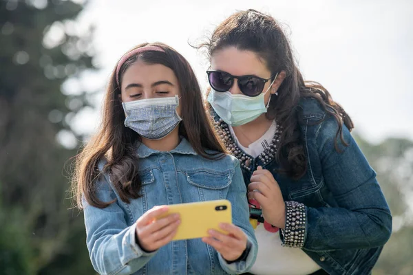 Две Молодые Девушки Рассматривают Фотографии Смартфоне Городском Парке Помощью Планшетов — стоковое фото