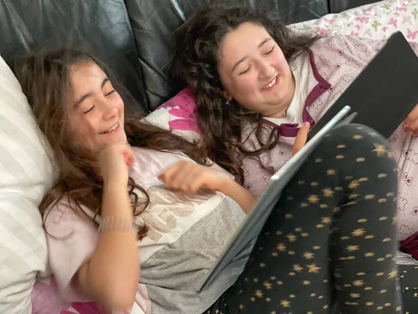 两个快乐的小女孩在沙发上玩平板电脑 — 图库照片