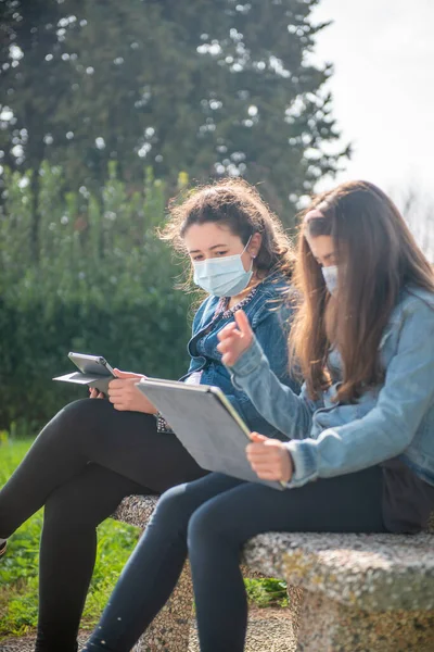Duas Meninas Sentadas Banco Parque Cidade Usando Tablets Usando Máscaras — Fotografia de Stock