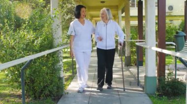 Asyalı doktor yaşlı kadına hastane bahçesindeki terasta yardım ediyor.