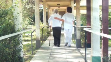 Asyalı kadın doktor, hastane bahçesindeki terasta yürüyen yaşlı kadına yardım ediyor.