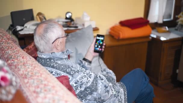 Elderly man using smartphone at home seated on the sofa — Stock Video