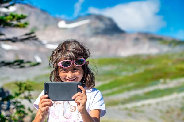 Happy young girl on a mountain trail holding smartphone making pictures.