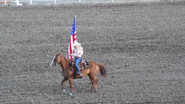 Κορίτσι με καπέλο καβάλα σε ένα άλογο ar Rodeo Park κρατώντας αμερικανική σημαία — Αρχείο Βίντεο