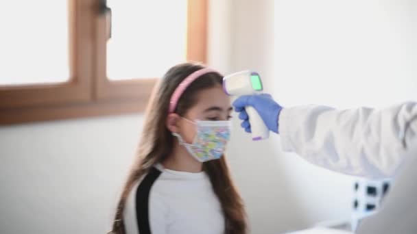 온도계를 가진 의사가 마스크를 쓰고 있는 두 어린 소녀에게 온도를 측정 한다 — 비디오