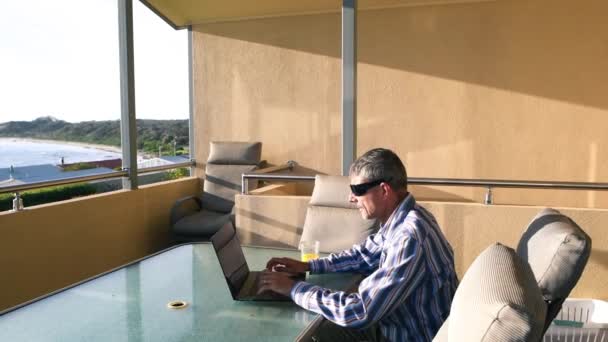 Hombre trabajando con su portátil en una hermosa terraza con vista al mar. Relax y concepto de negocio — Vídeos de Stock