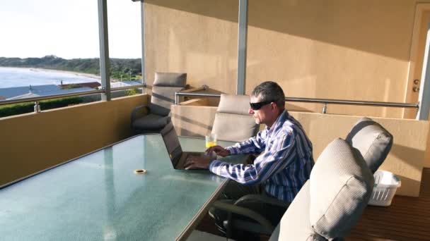 Ο άνθρωπος εργάζεται με το laptop του σε μια όμορφη βεράντα με θέα στον ωκεανό. Χαλαρώστε και επιχειρηματική ιδέα — Αρχείο Βίντεο