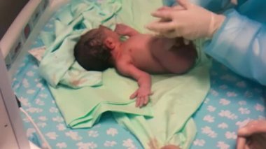 Doktor çocuk doktoru klinikte bebeği muayene ediyor, yeni doğmuş bebek yatakta ağlıyor.