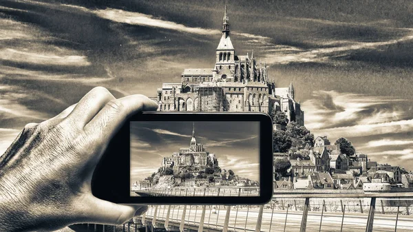 Female hand with smartphone taking a picture of Mont Saint Michel, France. Tourism concept.