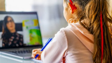 Erkek öğretmenin konuştuğu dizüstü bilgisayarında ders izleyen bir kız. Okul ve salgın zamanı