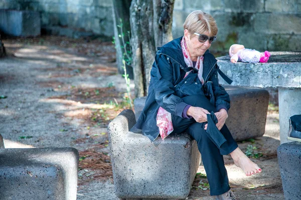 疲惫的老妇人把脚放在公共的城市长椅上休息 — 图库照片