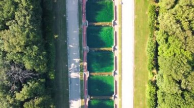 Reggia di Caserta 'daki havuzlar ve bahçeler. Yaz mevsiminde hareket eden bir drondan ağaçların ve suyun havadan görünüşü