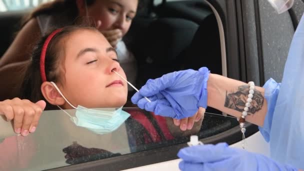 Pediatrician taking nasal mucus test sample from elementary age girls nose performing respiratory virus testing procedure at drive-thru — Stock Video