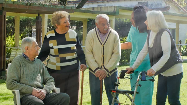 Dışarıda Rehabilitasyon Merkezinin Bahçesinde Yaşlı Çiftlerle Konuşan Afrikalı Bir Hemşire — Stok fotoğraf