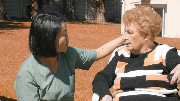 年轻的亚洲女医生安慰年老的退休妇女 在医院花园与她交谈 — 图库照片
