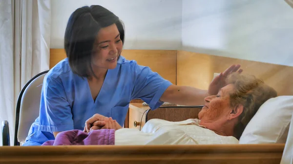 Νεαρή Ασιάτισσα Γιατρός Καθησυχάζει Ηλικιωμένη Συνταξιούχο Γυναίκα Στο Κρεβάτι Του — Φωτογραφία Αρχείου