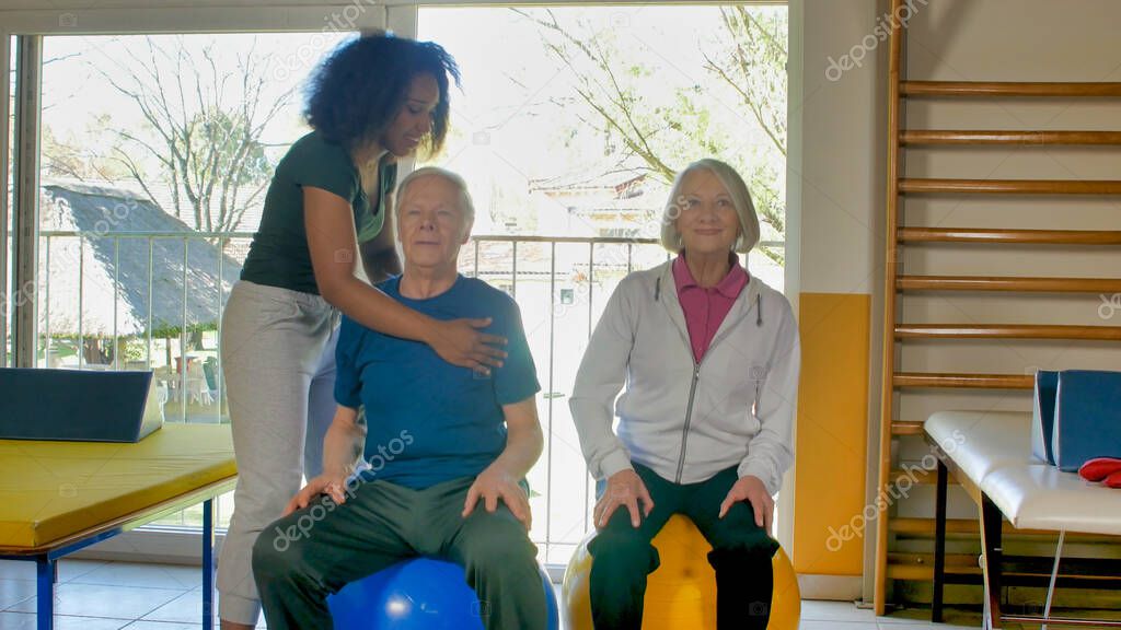 Rehabilitation concept. Elderly couple in a gym supervised by expert african female trainer.