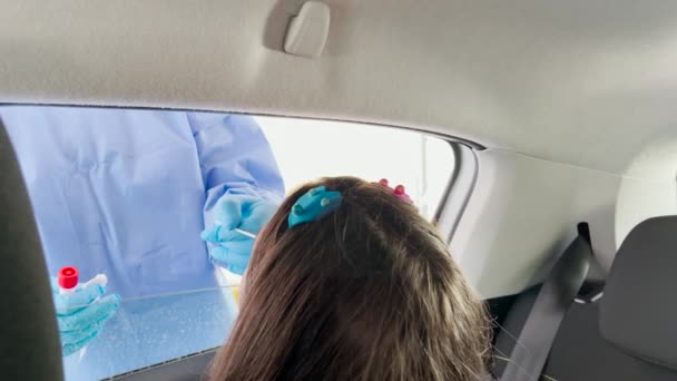 Врач в защитном костюме берет мазок из носа у молодой девушки, чтобы проверить на возможные ковидовые инфекции, задний вид в замедленной съемке — стоковое видео