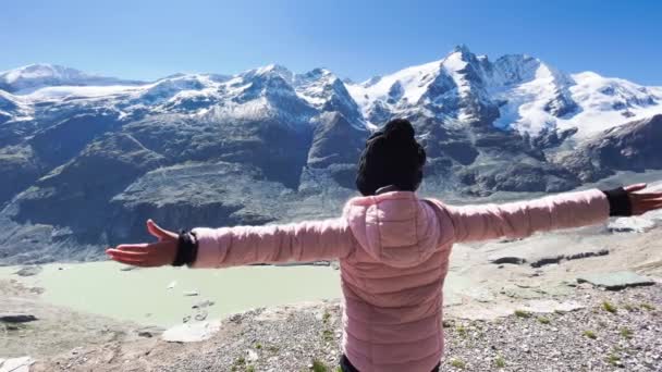 Погляд на молоду дівчину, яка обнімає свіже повітря з горами, вкритими снігом у літній сезон, Національний парк Гроссґлокнер (Австрія). — стокове відео
