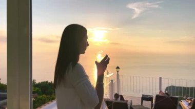 Yaz mevsiminde adanın arka planında gün batımında şarap içen kadın.