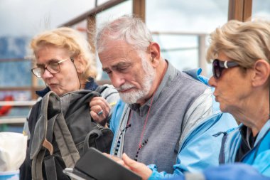 Yaşlı insanlar uzun bir dağ patikasından sonra bir barınak restoranının masasında dinleniyorlar.