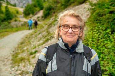 Mutlu yaşlı kadın bir dağ gezisinin ortasında dinleniyor.