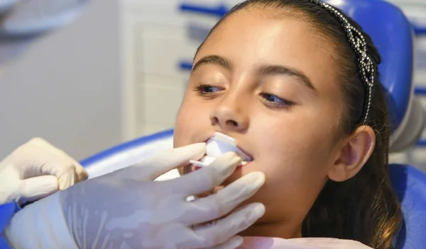 年轻的白人女性微笑着 而牙医戴着白色乳胶手套检查她的牙齿状况 坐在蓝色牙椅上的女婴 — 图库照片