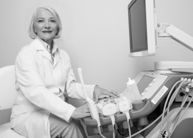 Senior female doctor smiling while setting up ultrasound machine clipart