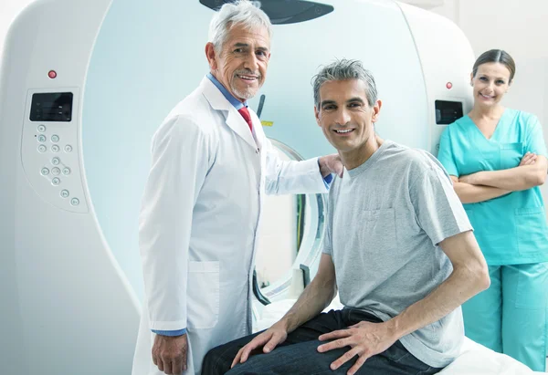 Mann in den Vierzigern bereit, sich einem MRI-Scan zu unterziehen, unterstützt von zwei lächelnden Männern. — Stockfoto