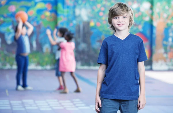 Niño feliz sonriendo en el patio de la escuela con otros niños jugando en —  Fotos de Stock