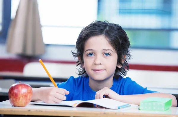 Kid i skolan skriver på sin bok med ett äpple på skrivbordet — Stockfoto