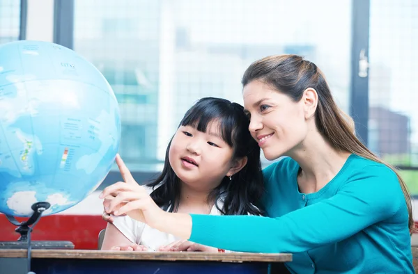 Primaria escuela profesora explicando Tierra globo a asiático mujer —  Fotos de Stock