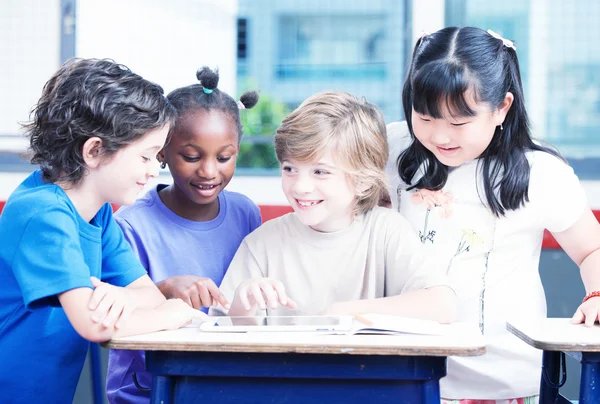 Счастливые многоэтнические ученики начальной школы за партой с таблицей и экзером — стоковое фото