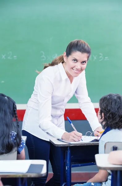 Ευτυχισμένος γυναίκας δασκάλας έλεγχος εργασίες μαθητών στο δημοτικό σχολείο — Φωτογραφία Αρχείου