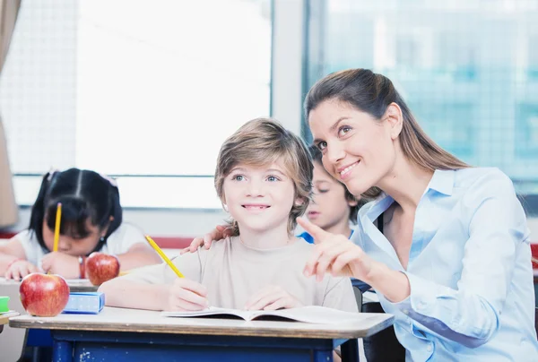 Lächelnde Lehrerin zeigt mit dem Finger auf etwas in der Schule — Stockfoto