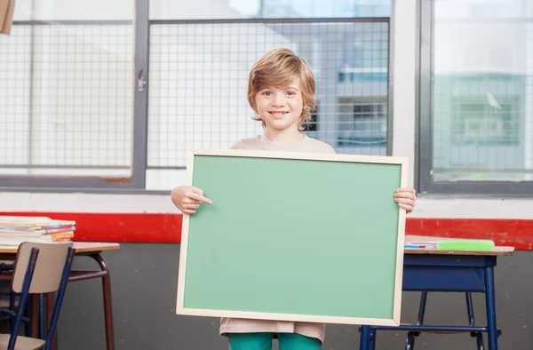 Schoolboy holding empty chalkboard in the classroom — Stock Photo, Image